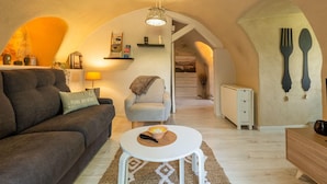 A cozy living room with a sofa, a small round table, and a chair. There is a staircase leading to an upper level.