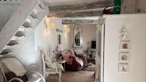A rustic room with a white staircase, a wicker chair, a sofa, and a white cabinet with a statue.