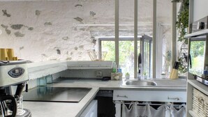 A kitchen with a stone wall, a coffee machine, a sink, and a window with plants.