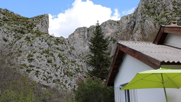 Una cabaña de montaña con techo inclinado, rodeada de terreno rocoso y vegetación escasa.