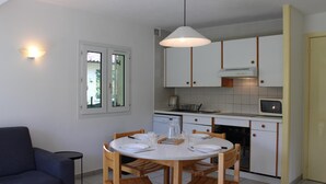 Una cocina compacta con armarios blancos, una mesa de comedor con sillas y una lámpara colgante.