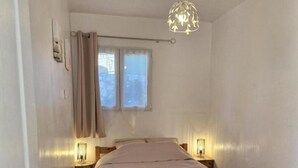 A bedroom with a wooden bed, two bedside lamps, a window with curtains, and a hanging light fixture. - Little House of Friends (LA GAUDE)