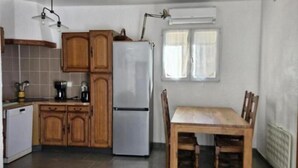 A compact kitchen with wooden cabinets, a refrigerator, a dining table with chairs, and a sofa. - Little House of Friends (LA GAUDE)