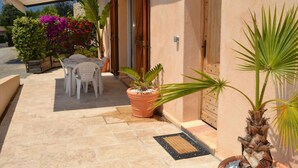 An outdoor patio area with a table and chairs, potted plants, and a door. - Little House of Friends (LA GAUDE)
