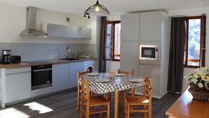Een moderne keuken met een eethoek, met een geruit tafelkleed, houten stoelen, een hanglamp en uitzicht op de omgeving.