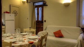 Zona pranzo con tavolo apparecchiato per quattro, un frigorifero bianco e un divano decorato con un cuscino arancione.
