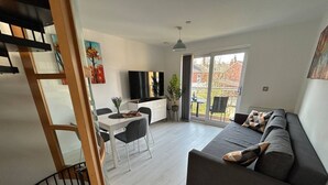 Ett modernt vardagsrum med en grå soffa, ett matbord med stolar, en tv och en balkong med utsikt.