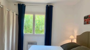 A bedroom with a bed, a window with curtains, a radiator, and a lamp. - Le Palmier - BENDEJUN (BENDEJUN)