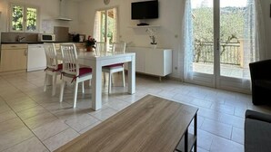 A spacious living area with a dining table, chairs, a TV mounted on the wall, and a balcony with sliding doors. - Le Palmier - BENDEJUN (BENDEJUN)