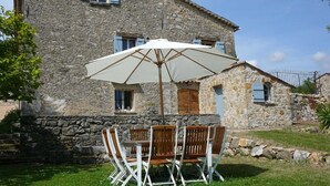 A stone building with a patio table and chairs, a white umbrella, and a stone wall. - Bastide de la Rousoulina (LE ROURET)