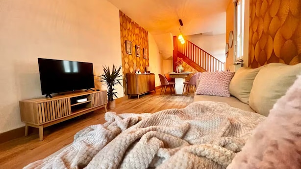 Un salon confortable avec un téléviseur à écran plat posé sur un meuble en bois, un coin repas avec une table et des chaises en bois, et un escalier avec une rampe en bois.