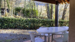 Un patio al aire libre con una mesa redonda y cuatro sillas, rodeado por una pérgola de madera y un seto.