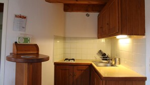 A compact kitchen with wooden cabinets, a small countertop, a radio, and a tiled backsplash.