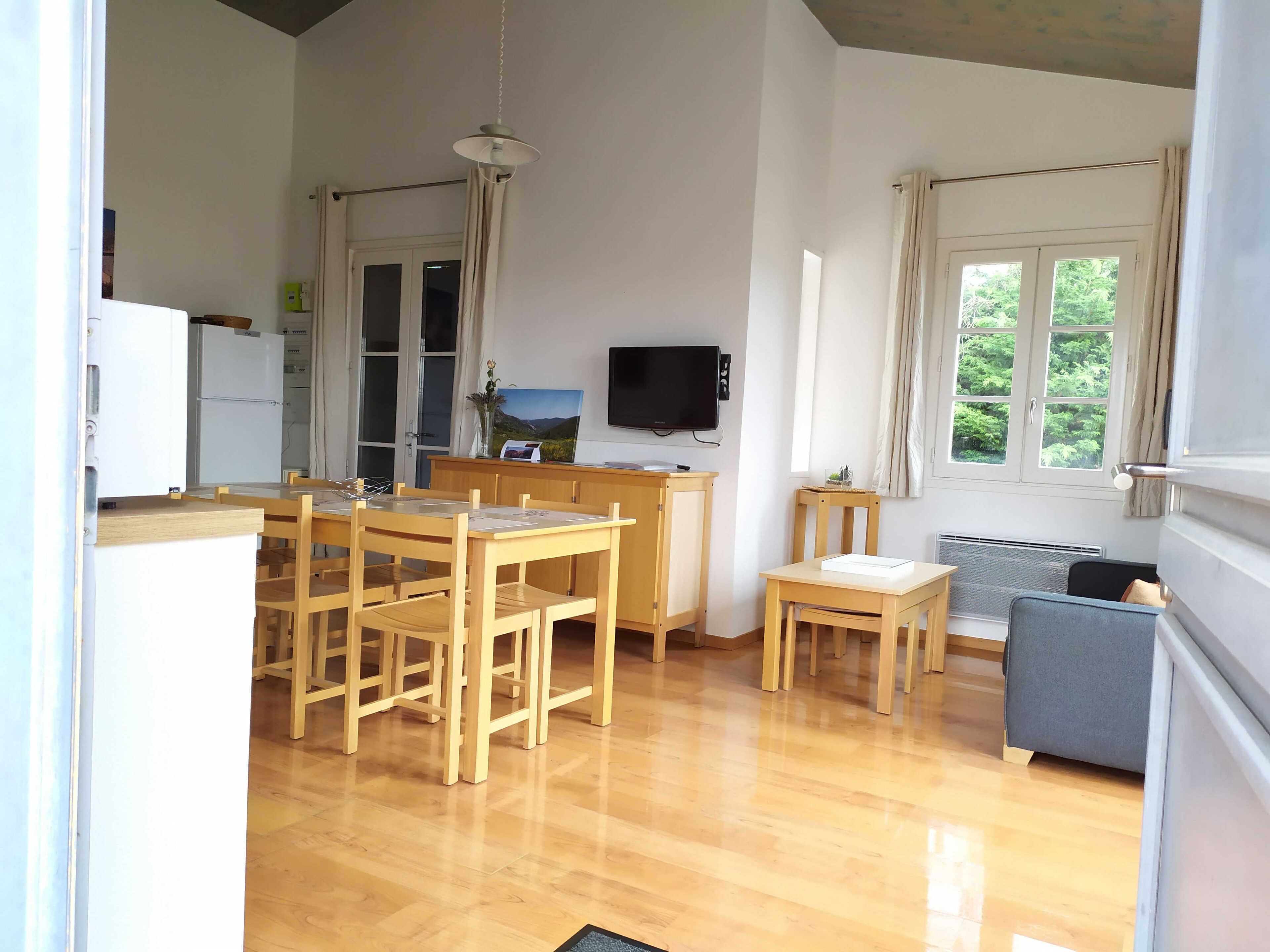 A compact kitchen with wooden furniture, a dining table, and a TV mounted on the wall.