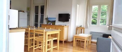 A compact kitchen with wooden furniture, a dining table, and a TV mounted on the wall.