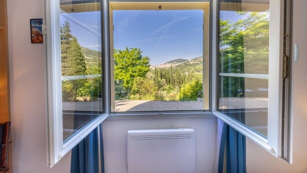A room with a large window offering a view of a green landscape with trees and hills.