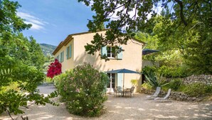 A two-story house with a patio area, a stone wall, and a gravel driveway.