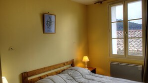 A bedroom with a bed, a bedside lamp, a window with a view of a tiled roof, and a framed botanical illustration on the wall. - Saint-Roch - PEILLE - Gîte (PEILLE)