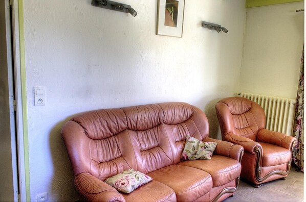 Una habitación con un sofá y un sillón de cuero marrón, un radiador y un cuadro en la pared.