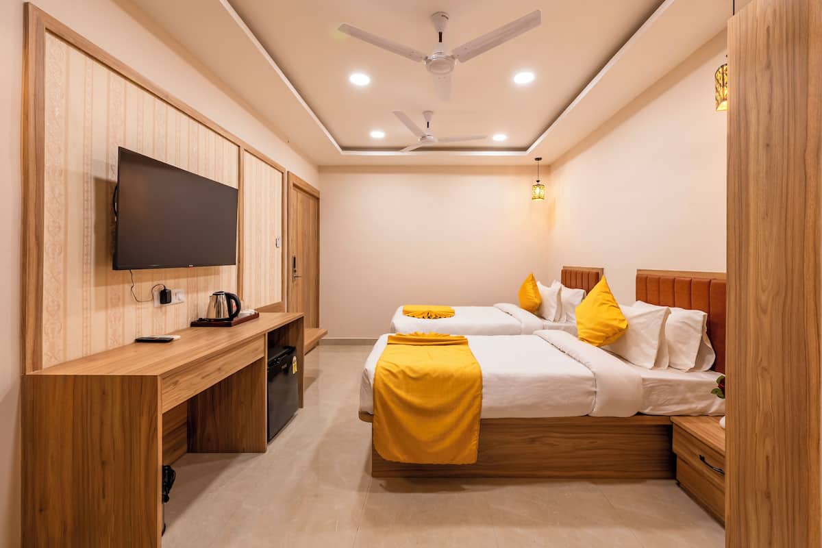 A hotel room with two beds, a TV, a desk, and a ceiling fan.