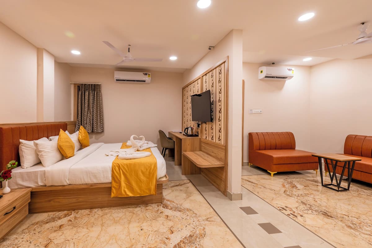 A modern hotel room with a bed, a desk, a sofa, and a TV.