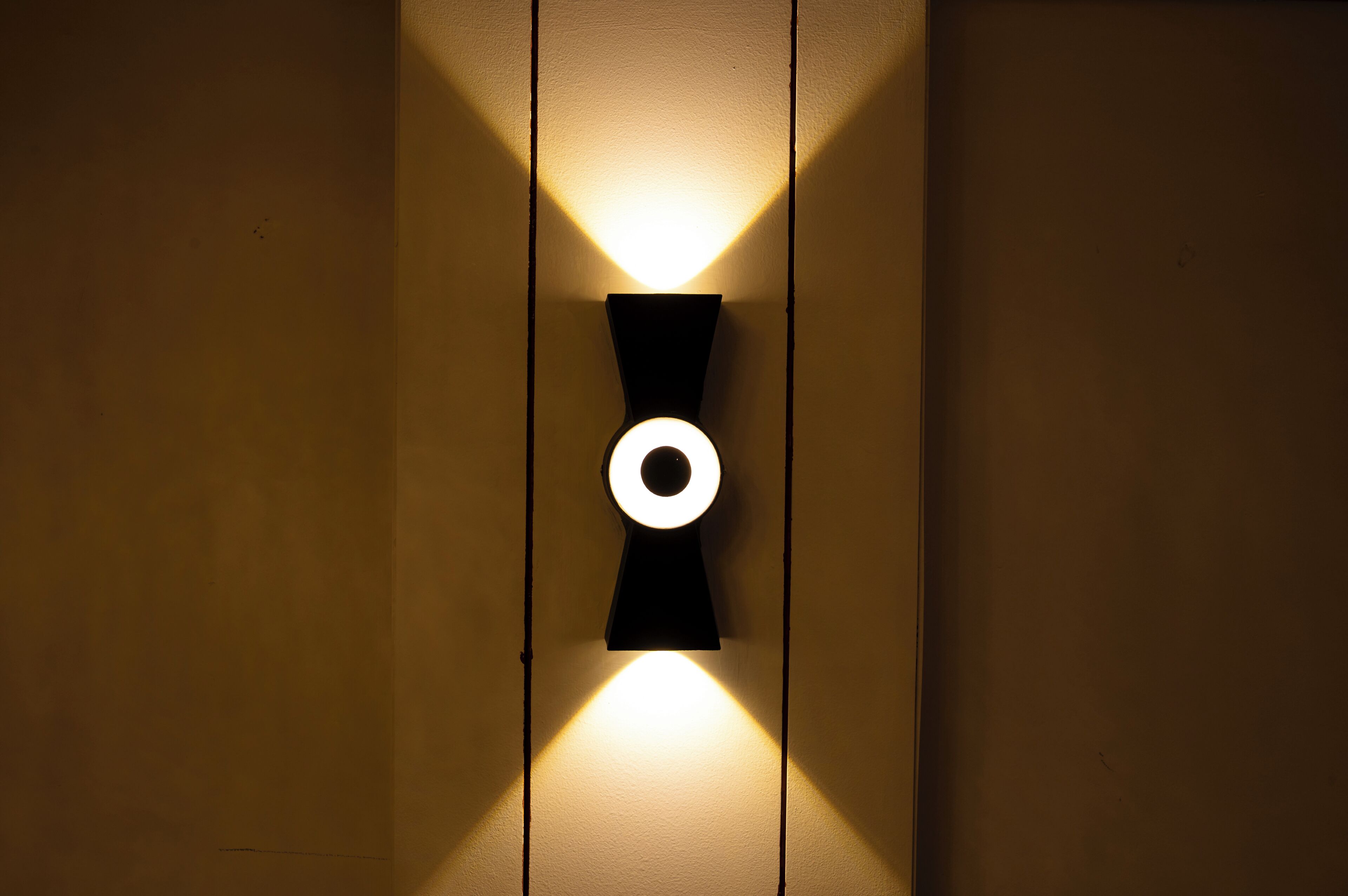 A wall-mounted light fixture with a circular design and a central ring, casting a warm glow on the wall.