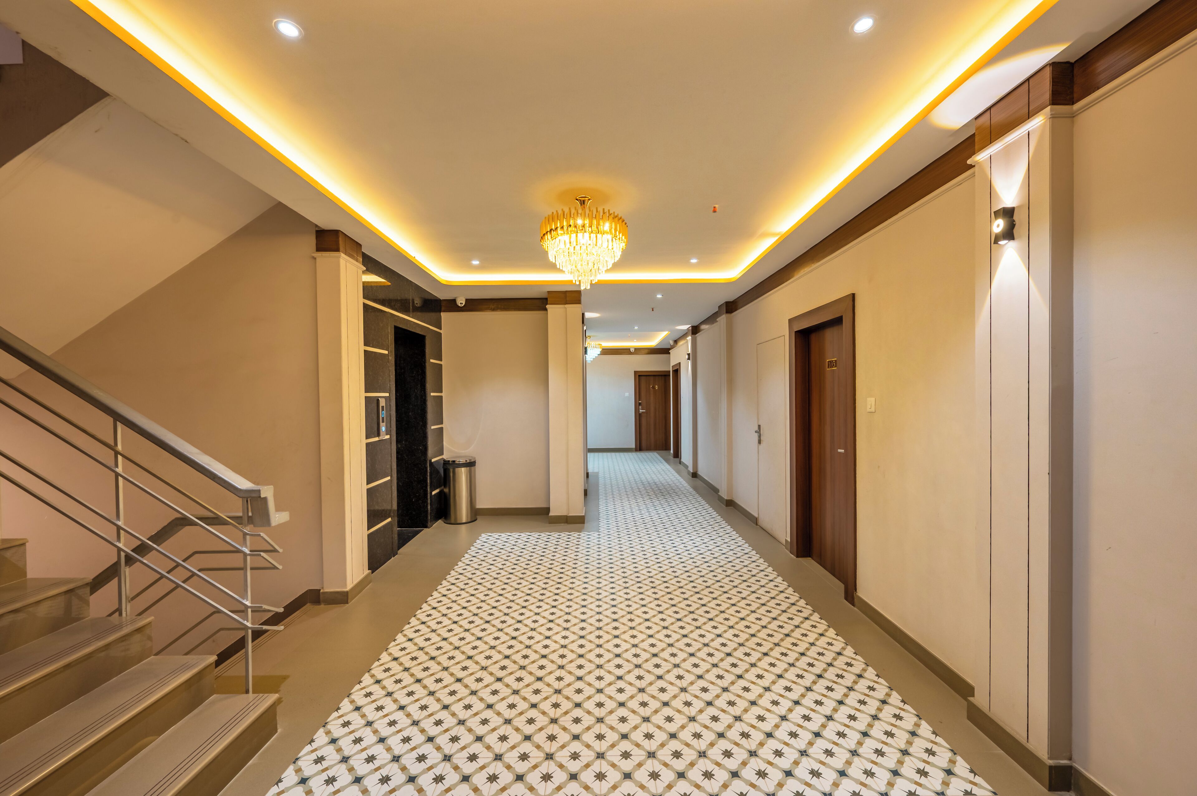 A hotel hallway with a patterned floor, a chandelier, and a staircase.