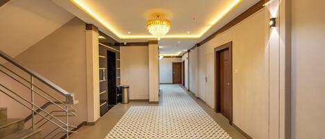A hotel hallway with a patterned floor, a chandelier, and a staircase.
