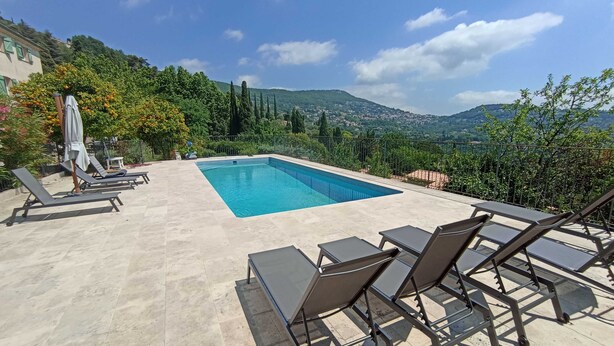 Ein rechteckiger Pool mit glasklarer, blauer Wasseroberfläche, umgeben von einer gefliesten Terrasse mit Liegestühlen und einem Tisch.