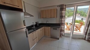 Eine moderne Küche mit Holzausstattung, einem Edelstahlkühlschrank und einem Geschirrspüler. Ein Glastür öffnet sich zum Außenbereich mit einer Terrasse, einem Tisch und Stühlen.