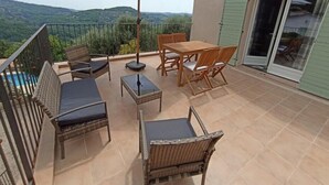 Ein Balkon mit Tisch und Stühlen, einem großen Sonnenschirm und Blick auf die Hügel.