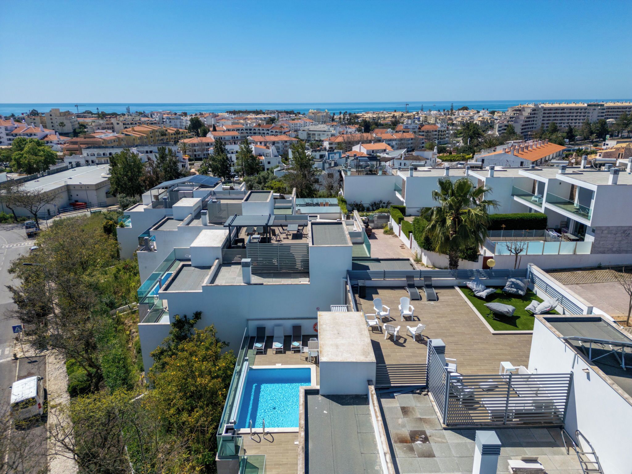 A rooftop pool area with lounge chairs and a swimming pool, surrounded by modern buildings and a view of the sea.