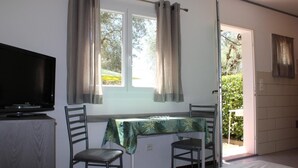 A room with a bed, a television, a window with curtains, a table with a tablecloth, and a chair. - Riola Farm - Gîte n°6004 (Contes)