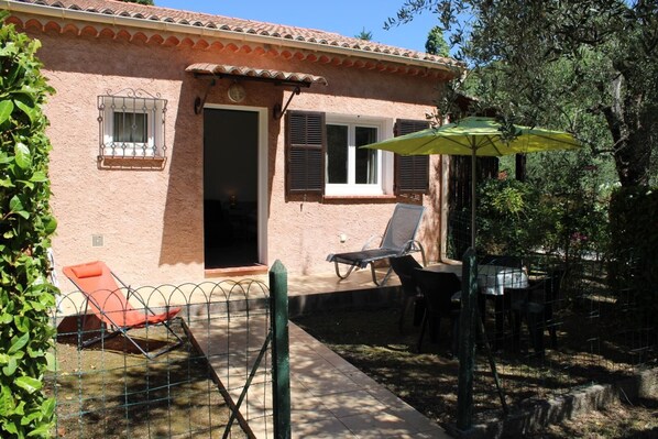 A house with a patio, a chair, a table, and a green umbrella.