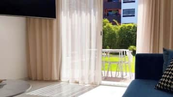 Un salon moderne avec un canapé bleu, un téléviseur à écran plat fixé au mur et une porte-fenêtre coulissante donnant sur un espace extérieur équipé d’une table et de chaises.
