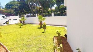 A well-maintained garden with a lawn, several small trees, and a white wall in the background. - Luxury Villa Hay Ryad (Rabat)
