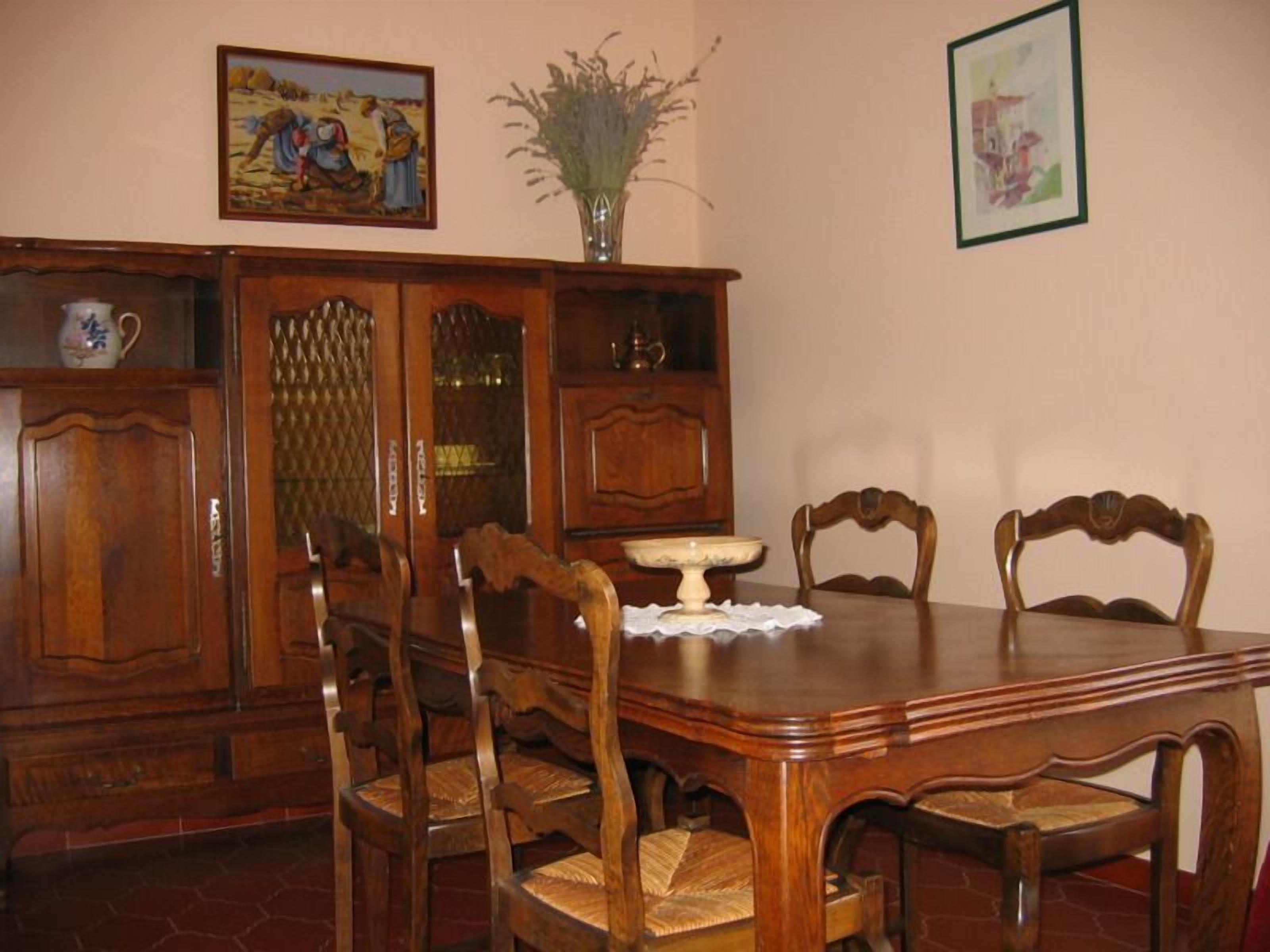 Ein Esszimmer mit einem Holztisch, vier Stühlen, einer Blumenvase und zwei gerahmten Bildern an der Wand.