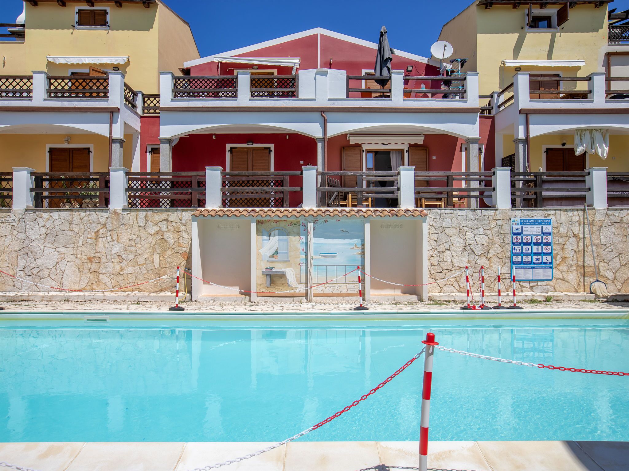 A swimming pool with a stone wall and a building with balconies in the background.