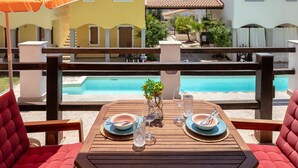 A poolside dining area with wooden tables and red cushioned chairs, overlooking a pool and adjacent buildings. - Luce del Mare by Interhome (Valledoria)