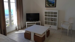 A living room with a TV, a bookshelf, a table, and a chair. - Romarin - EZE - Gîte (EZE)