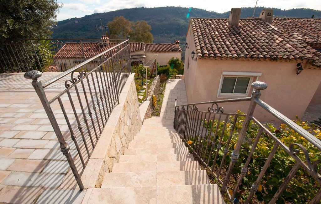 A staircase leading to a building with a tiled roof, surrounded by greenery and a mountainous backdrop.