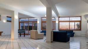 Amplia sala de estar con mesa de billar, dos sofás y ventanas grandes que ofrecen vistas al exterior.
