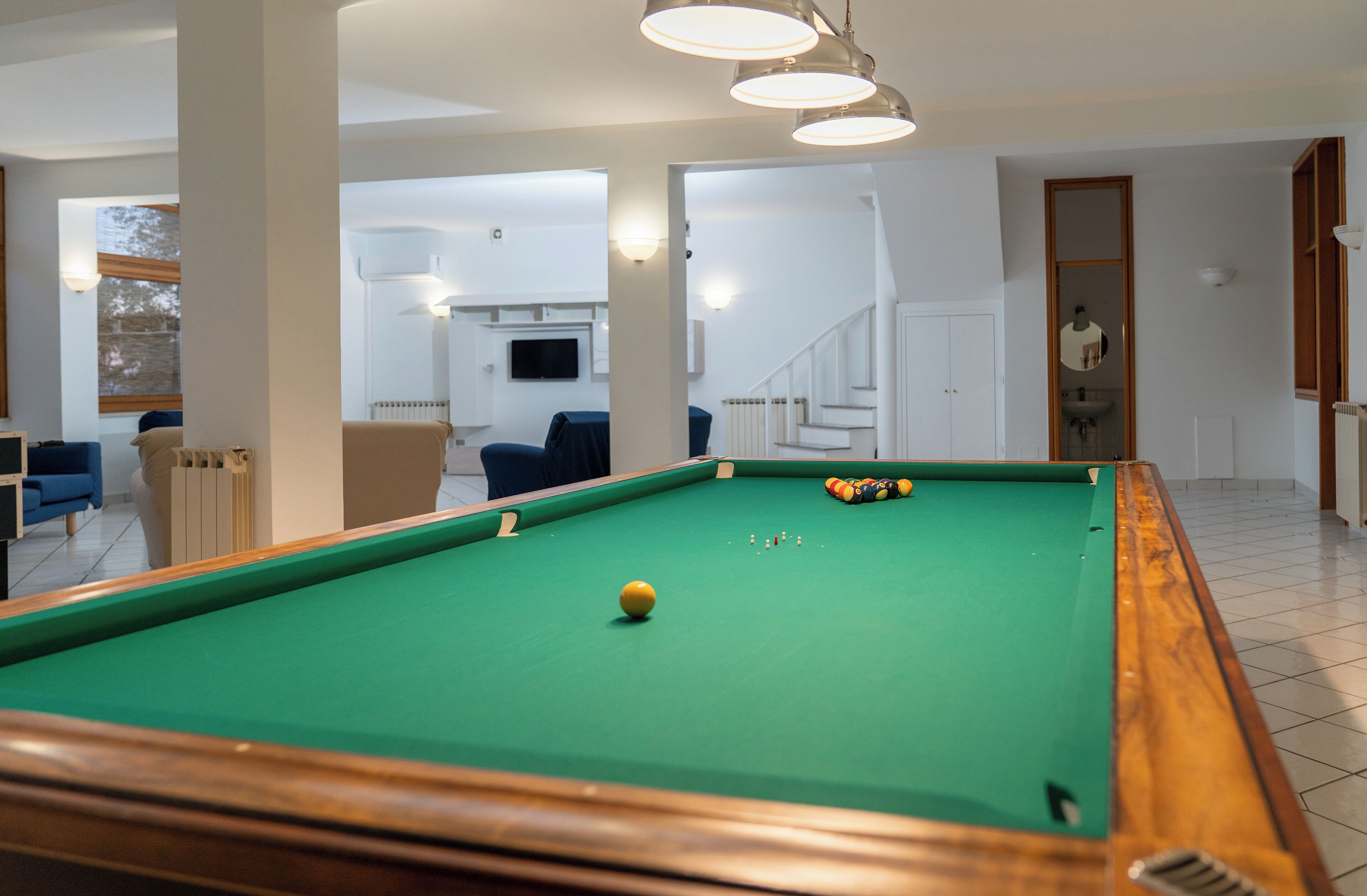 Uma mesa de bilhar em um espaço com vista para uma escadaria e uma sala de estar.