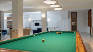 Una mesa de billar en una habitación con vista a una escalera y una sala de estar.