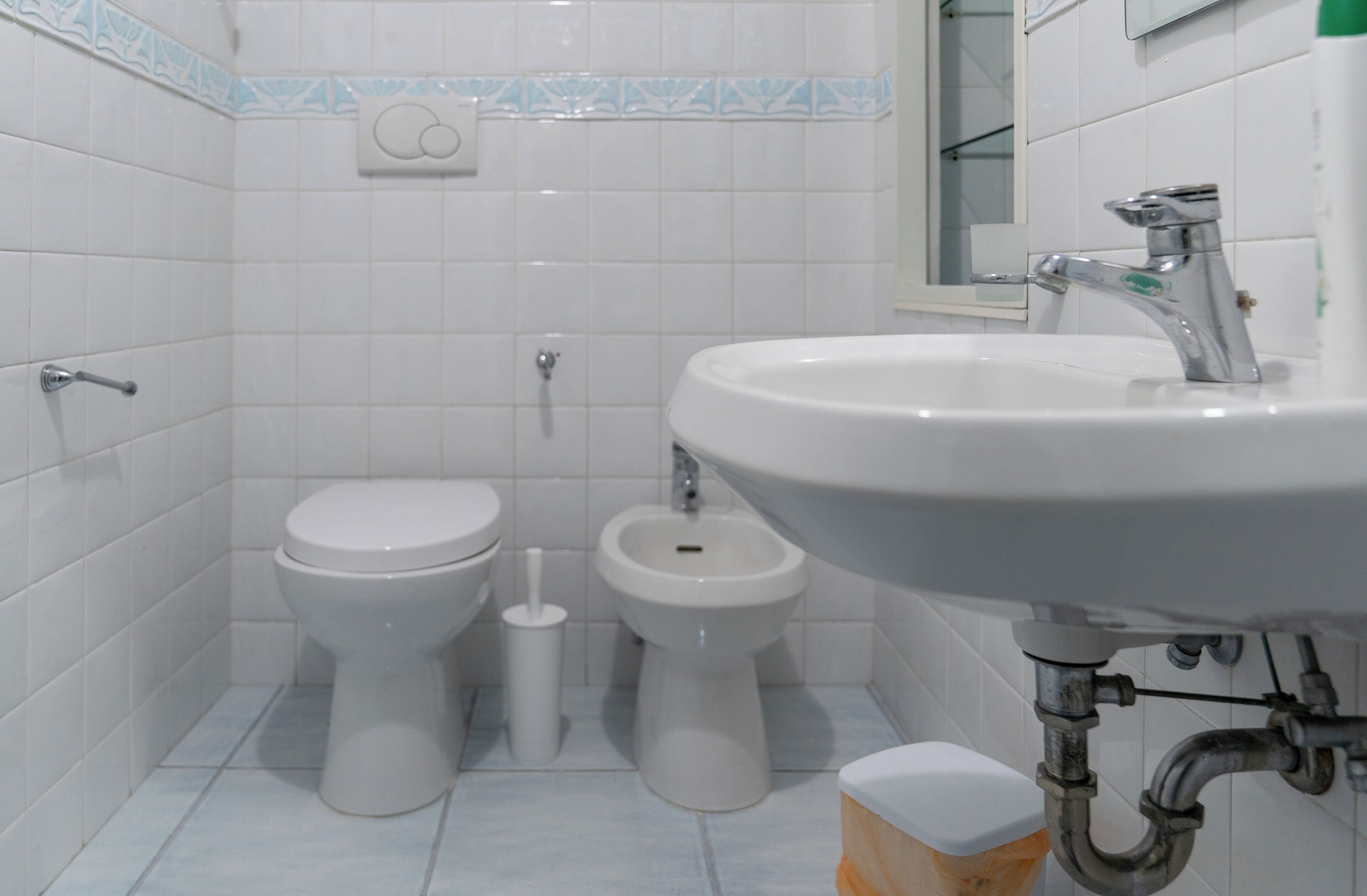 A bathroom with two toilets, a bidet, a sink, and a mirror.