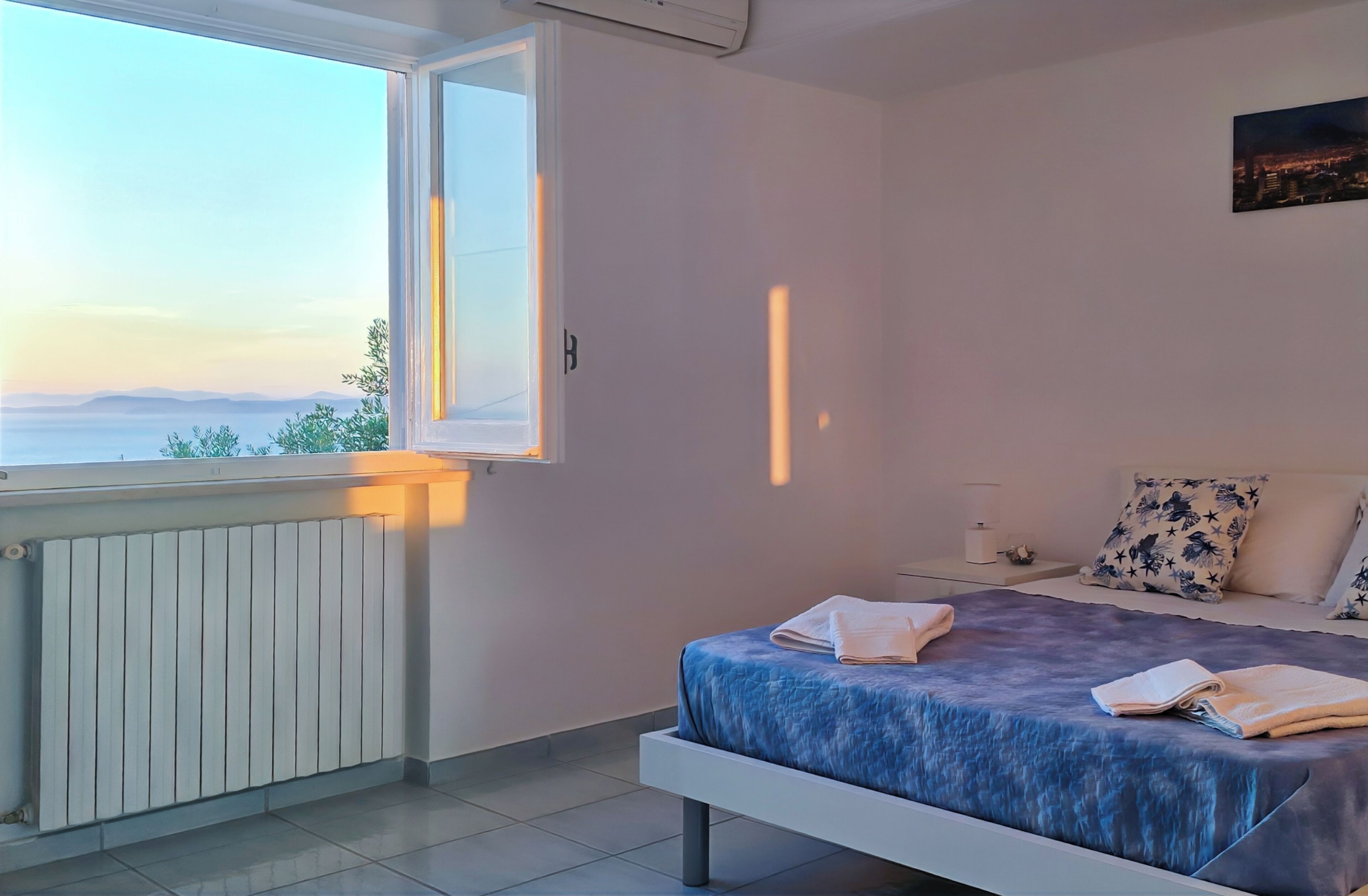 Quarto com cama, mesa de cabeceira, janela com vista e radiador.