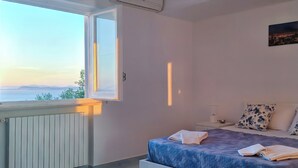 Un dormitorio con cama, mesita de noche, radiador y ventana con vistas abiertas.