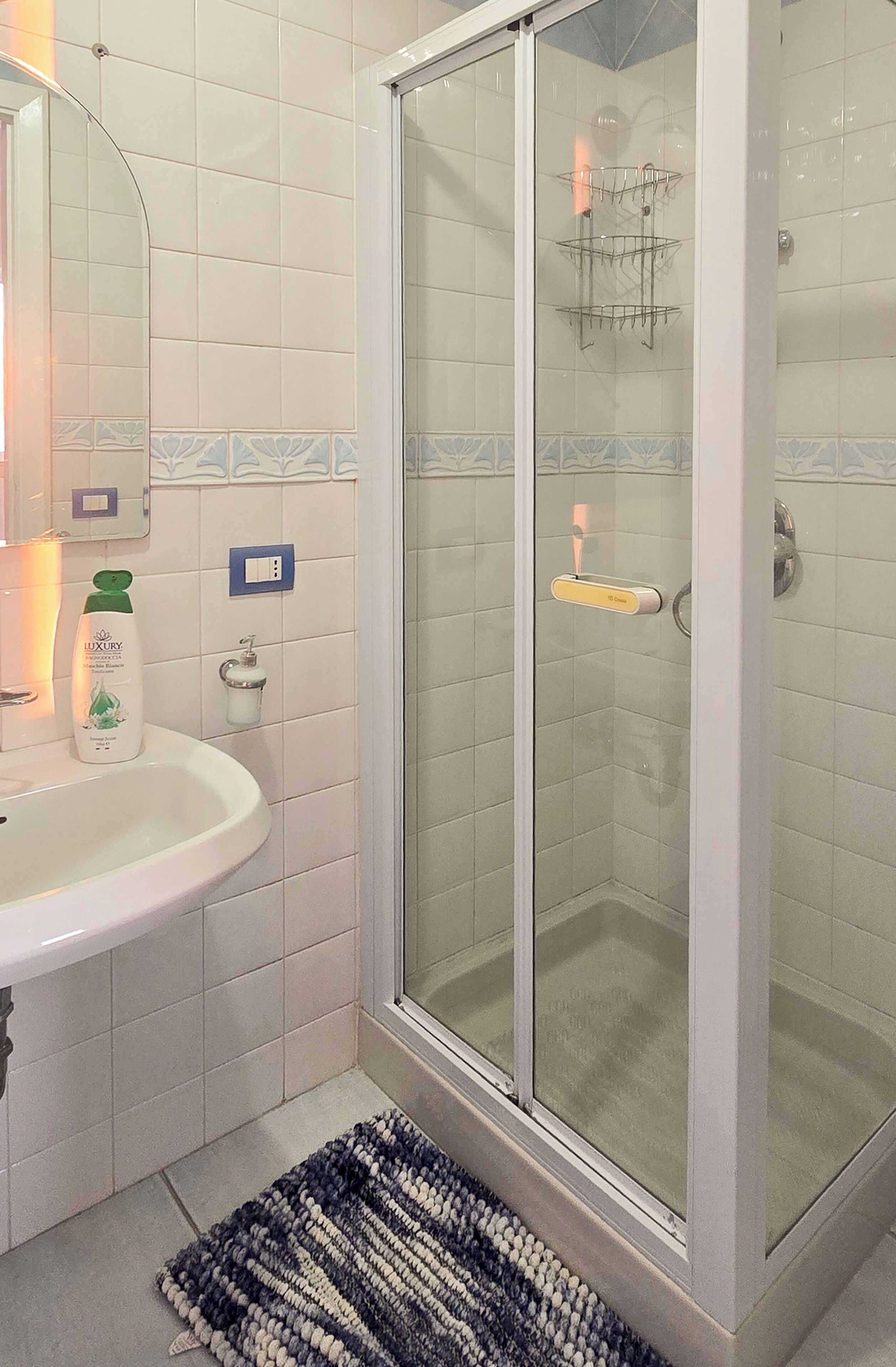 A bathroom with a white sink, a glass shower enclosure, and a blue and white patterned rug.