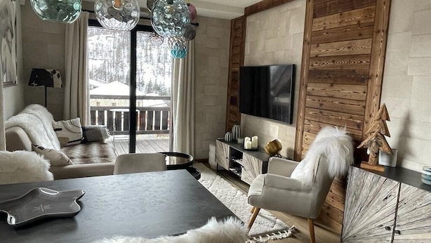 Una sala de estar moderna con un panel de pared de madera, un televisor de pantalla plana y un ventanal con vistas a un paisaje nevado.