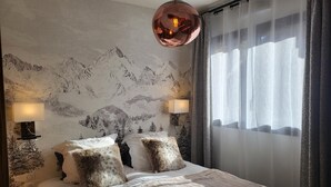 Un dormitorio con papel tapiz de temática montañosa, una cama grande con almohadas mullidas, dos lámparas de noche y cortinas translúcidas.